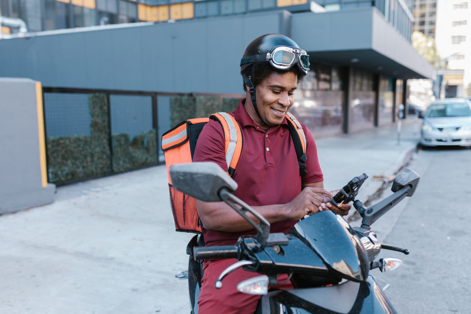 A delivery rider sitting on his motorcycle, smiling as he checks his phone.